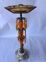 Front view of ashtray showing amber glass dish, column, hanging prisms, ornate base