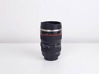 Front angle view of camera lens tumbler mug showing details such as lens markings, focus and zoom rings, and a lid designed to resemble a lens hood.