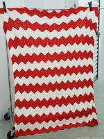 Full view of the red and white crocheted tablecloth hanging on a metal rack, showing the chevron zigzag pattern and overall size.