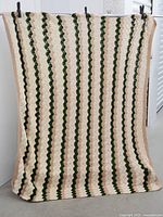 Full view of crocheted tablecloth hanging showing stripes of green, beige and white crochet.