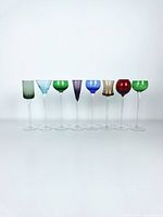 Front view of 8 assorted colored long stem liqueur glasses in a row on white background.