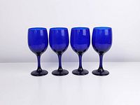 Four blue cobalt tall iced tea glasses shown side by side on white background.