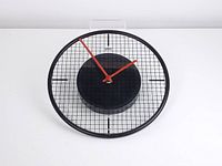 Front view of Umbra Memphis style wall clock showing black rubber rim, glass face with grid, and red hands.