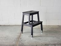 Side angle view of the step ladder stool showing two steps and caster wheels.