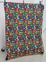Full view of the camouflage patterned throw blanket hanging on a clothes rack, showing the multicolor camouflage pattern and brown edges.