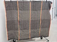Full view of throw blanket showing black and grey plaid pattern with vertical yellow and red lines, fringed edges.
