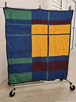 Full view of vintage wool throw blanket showing large plaid blocks in yellow, blue, green, and dark red with black binding edge.