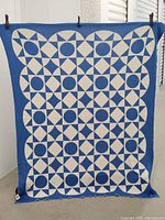 Blue and white geometric patterned throw blanket hanging to show one side with blue border and mostly white background.