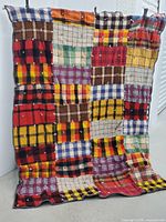 Full view of wool patchwork throw blanket hanging, shows multiple colorful plaid wool patches sewn together.