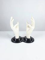 Front view of two white hand mannequins on black base against plain background
