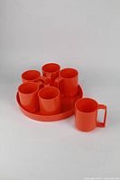 Six vintage orange plastic mugs arranged on matching round tray, one mug placed beside the tray. All with smooth finish and no chips or cracks.