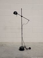 Full view of the black post-modern floor lamp with round base and adjustable arm.