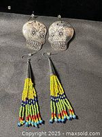 Front view of both earring pairs—metal skulls and beaded fringe