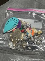 Bag with visible turquoise cut-out teardrop, gold disc, faux pearls, chains and other single earrings