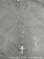 Full view of silver-tone necklace and cross pendant on textured background
