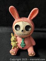 front view of stitched pink bunny coin bank with skull face and small plush held