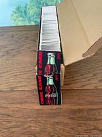 Open cardboard box filled with vertically stacked 1999 Coke Cards showing front design