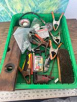 Overview of green bin containing wooden level, clamps, brush, gauge, hardware