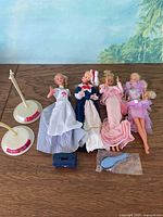Four Barbie dolls with stands and accessories displayed on tabletop