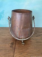 Front view of tapered copper pot, handle raised, shows oxidation and front dent