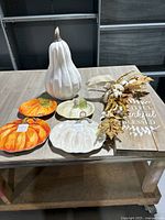 Group shot of pumpkin figurine, three plates and wooden sign with foliage