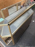 Oblique top view of glass display case showing gold frame, glass panels, mirrored front