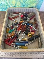 Gray bin filled with assorted screwdrivers showing quantity and variety