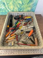 Top view of entire lot in bin showing screwdrivers, tape measure, wire stripper, cleaning brush, bits and hardware