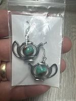 Front view of the pair of teapot earrings in plastic bag, showing design and stones