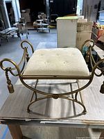 Full view front angle of gold metal vanity stool showing rope arms and tassels