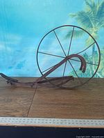 Full view of rusted iron push plow with large spoked wheel and frame