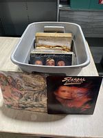 Grey plastic bin filled with upright vinyl LP records, two records displayed in front