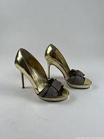 Three-quarter front view showing gold patent leather, ribbon bow, heel height