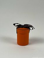 Orange cylindrical Hermès box with black ribbon