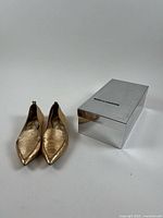 Pair of gold Nicholas Kirkwood Beya shoes beside mirrored box