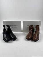 Two pairs of ankle boots, black and brown, with branded boxes