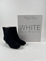 Pair of black suede wedge ankle boots in front of branded box