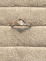 Front view of sterling silver ring displaying swirl bypass design and clear round stone