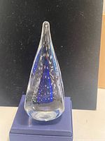 Front view of teardrop glass paperweight on box displaying blue core and bubble pattern
