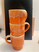 Three orange drip glaze stacking mugs shown stacked
