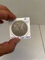 Reverse view of the 1921 Morgan Silver Dollar in cardboard holder showing eagle and inscriptions including year '1921' and handwritten notes on holder.