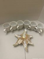 Six white porcelain coffee mugs arranged in two rows and the iridescent starfish-shaped glass dish placed in front.