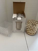 Photo showing two Bowring glass pieces: textured glass cube and boxed ribbed vase, next to gold-tone ornament with pearl mesh.