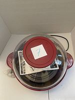 Top view of red Popflix electric popcorn maker showing clear dome lid, instruction manual inside, and power cord wrapped beside it.