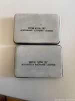 Two rectangular metal cases with engraved text 'HIGH QUALITY AUSTRALIAN SOUVENIR LIGHTER' shown closed.
