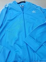 Front view of blue Adidas track jacket laid flat