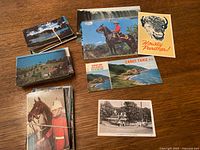 Several bundled stacks of Canadian postcards spread on tabletop, showing horse rider, buffalo graphic, Cabot Trail scenic view, black-and-white inn image