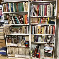 Two tall white bookcases filled with vintage cookbooks and recipe files