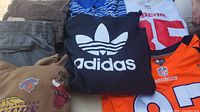 Pile showing pants, striped polo, Adidas sweatshirt, 49ers and Broncos jerseys