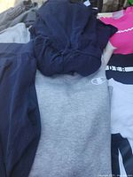 Pile showing navy hoodie over grey Champion sweatshirt, pink top and black/white tee